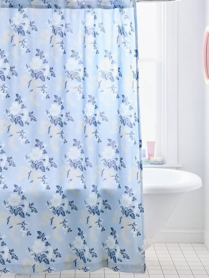 A light blue shower curtain with a dense, repeating floral pattern printed in white, navy blue, and pale yellow accents.