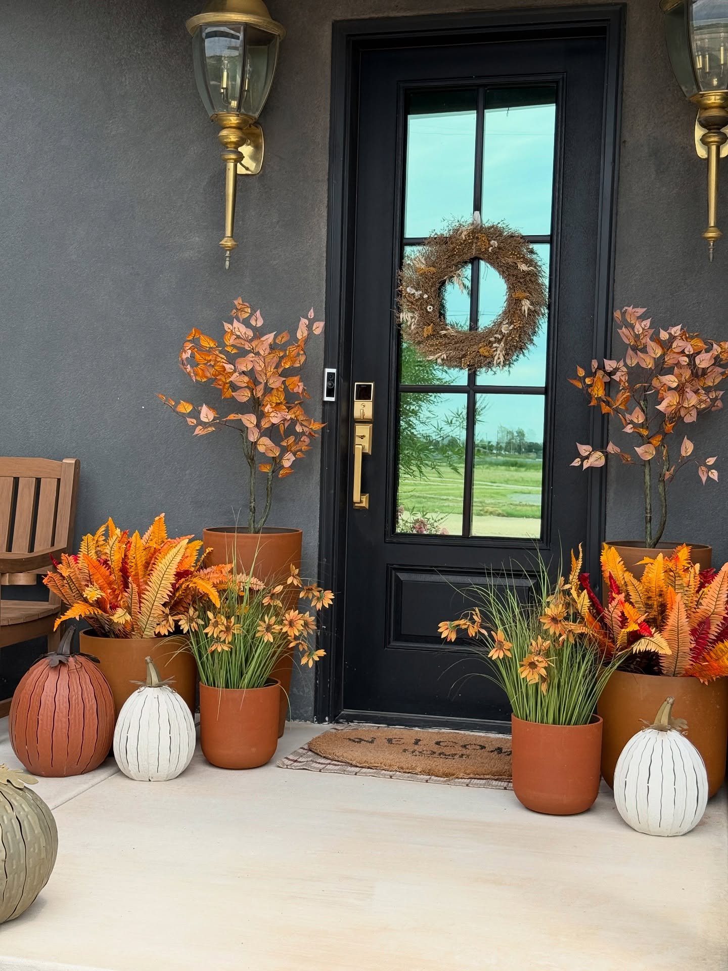 A contemporary porch with a dark gray wall, decorated with a terracotta-toned mix of pumpkins, planters, and autumnal foliage.