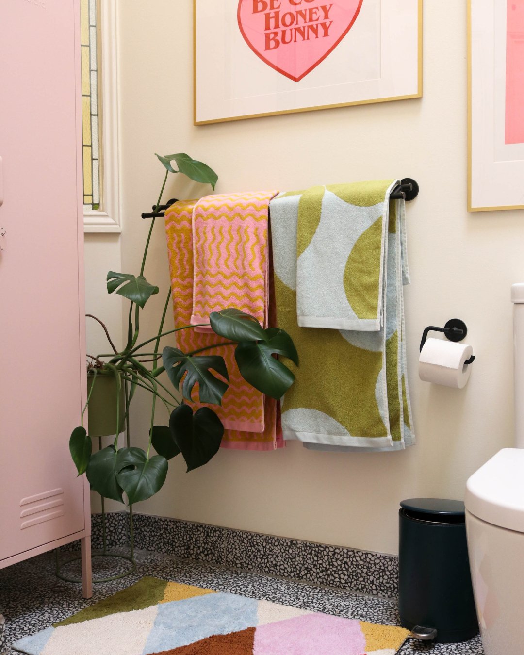 Two brightly colored, patterned towels pink zig-zag and green abstract—hanging in an eclectic, modern bathroom.