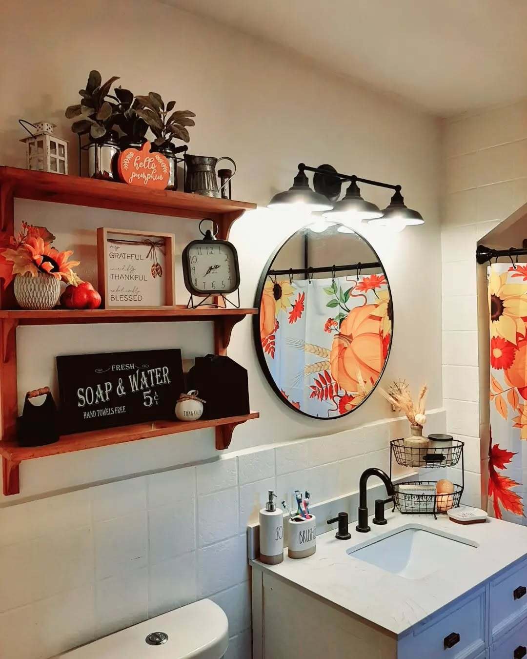A bathroom with wooden floating shelves filled with a variety of fall decorations, a pumpkin and leaf-themed shower curtain.