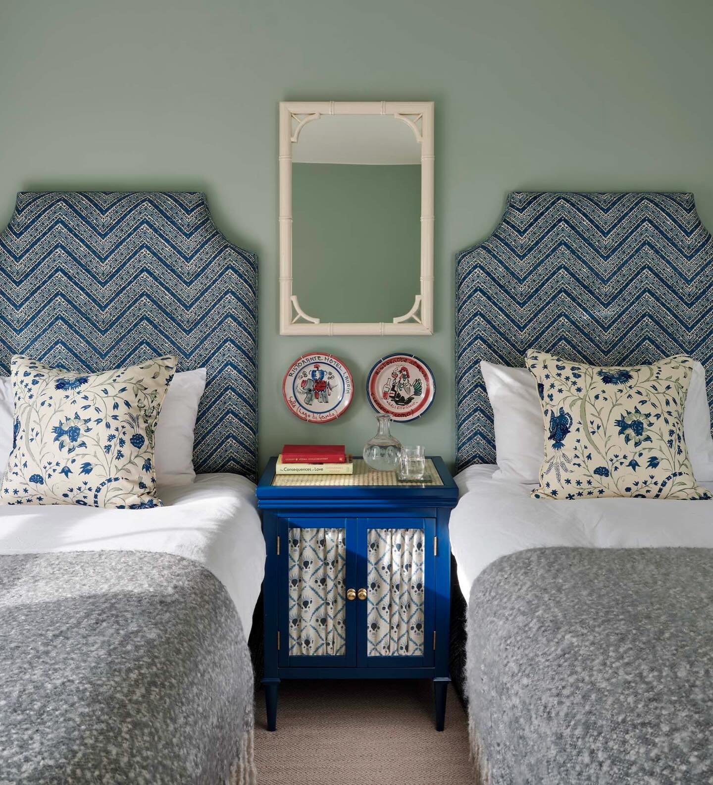 An eclectic twin bedroom with two beds, blue and white chevron headboards, and a bright blue nightstand.