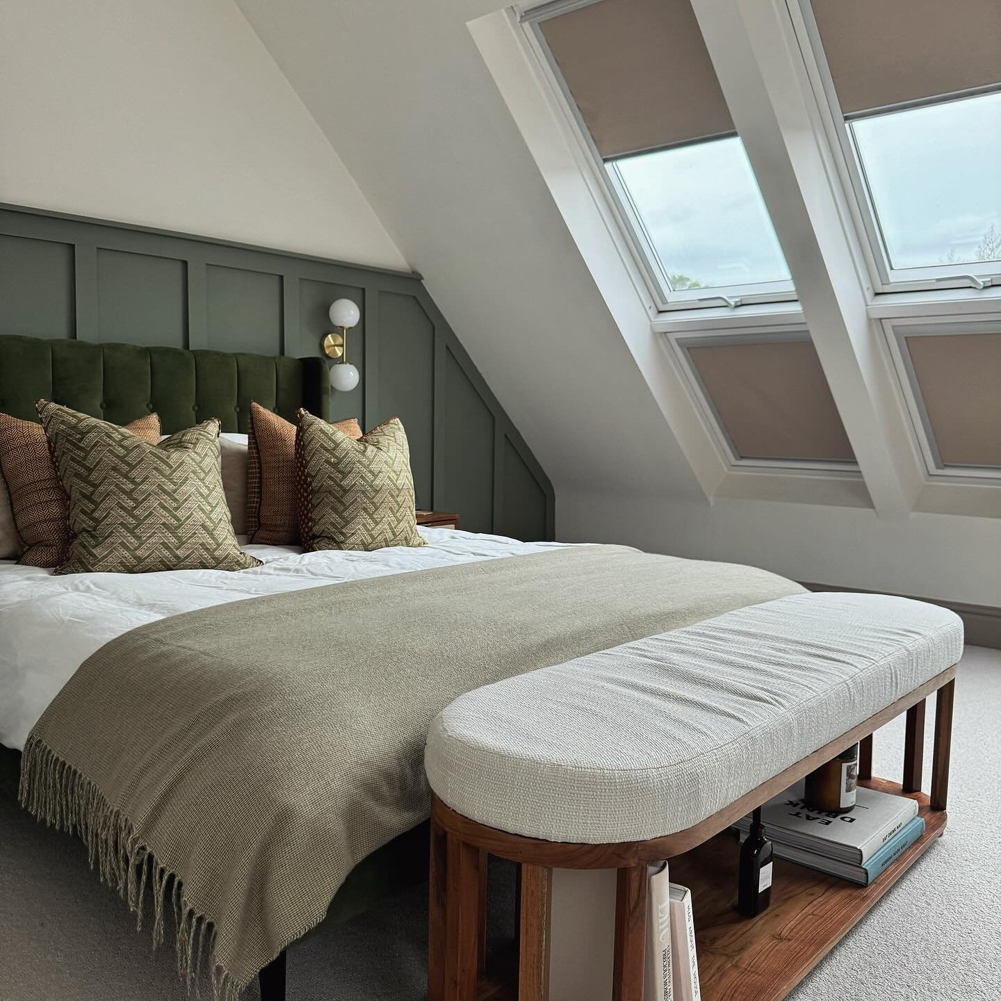 A modern loft bedroom with a dark green paneled accent wall, a green velvet bed, and a wooden bench at the foot.