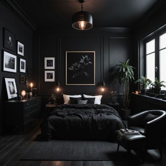 A dark, moody bedroom with all-black walls and wainscoting, a large bed with black bedding, a gallery wall of art, and various plants.