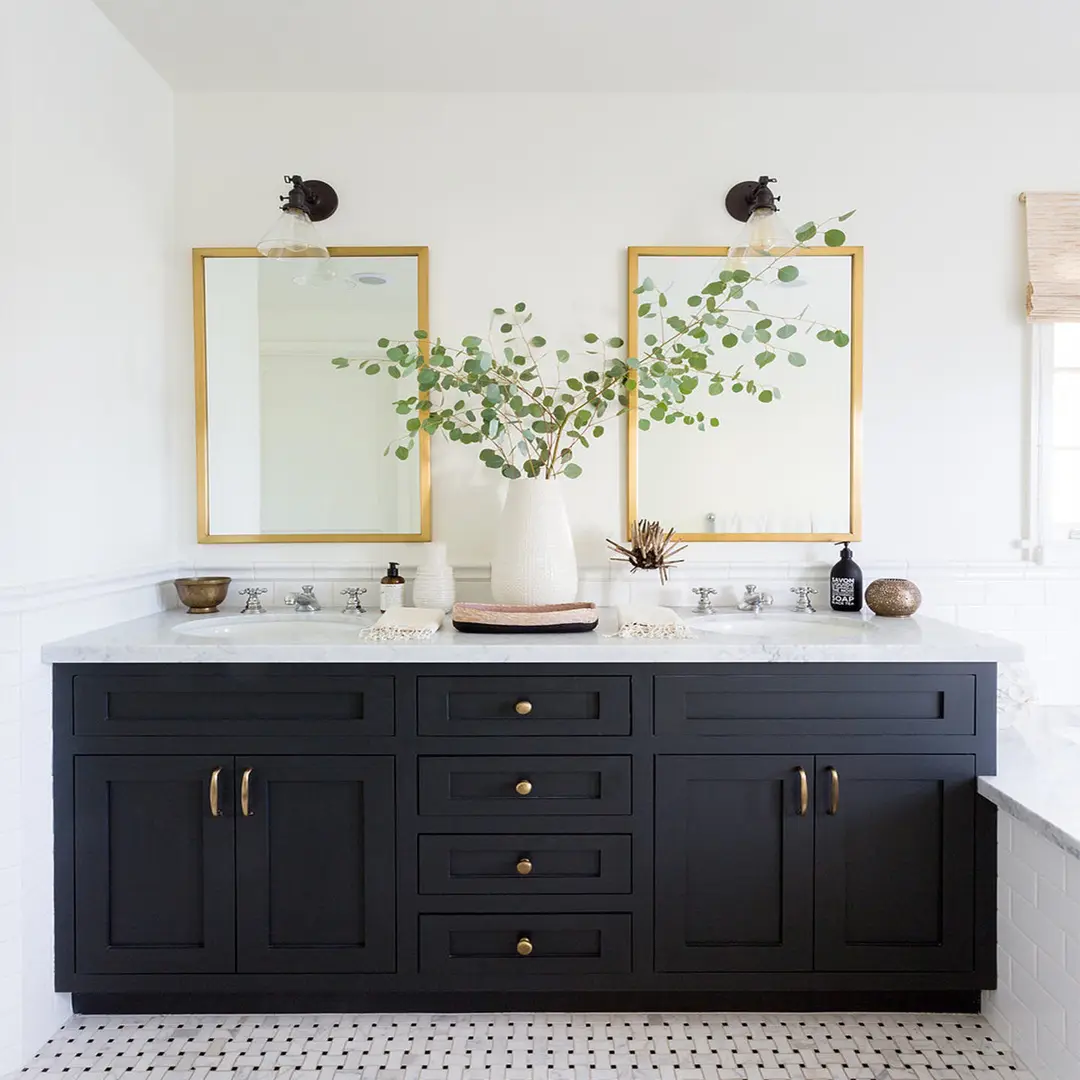 A dark gray-blue farmhouse-style double vanity with gold pulls and a white marble countertop. It features two sinks and is paired with two separate gold-framed rectangular mirrors and twin wall-mounted sconces.