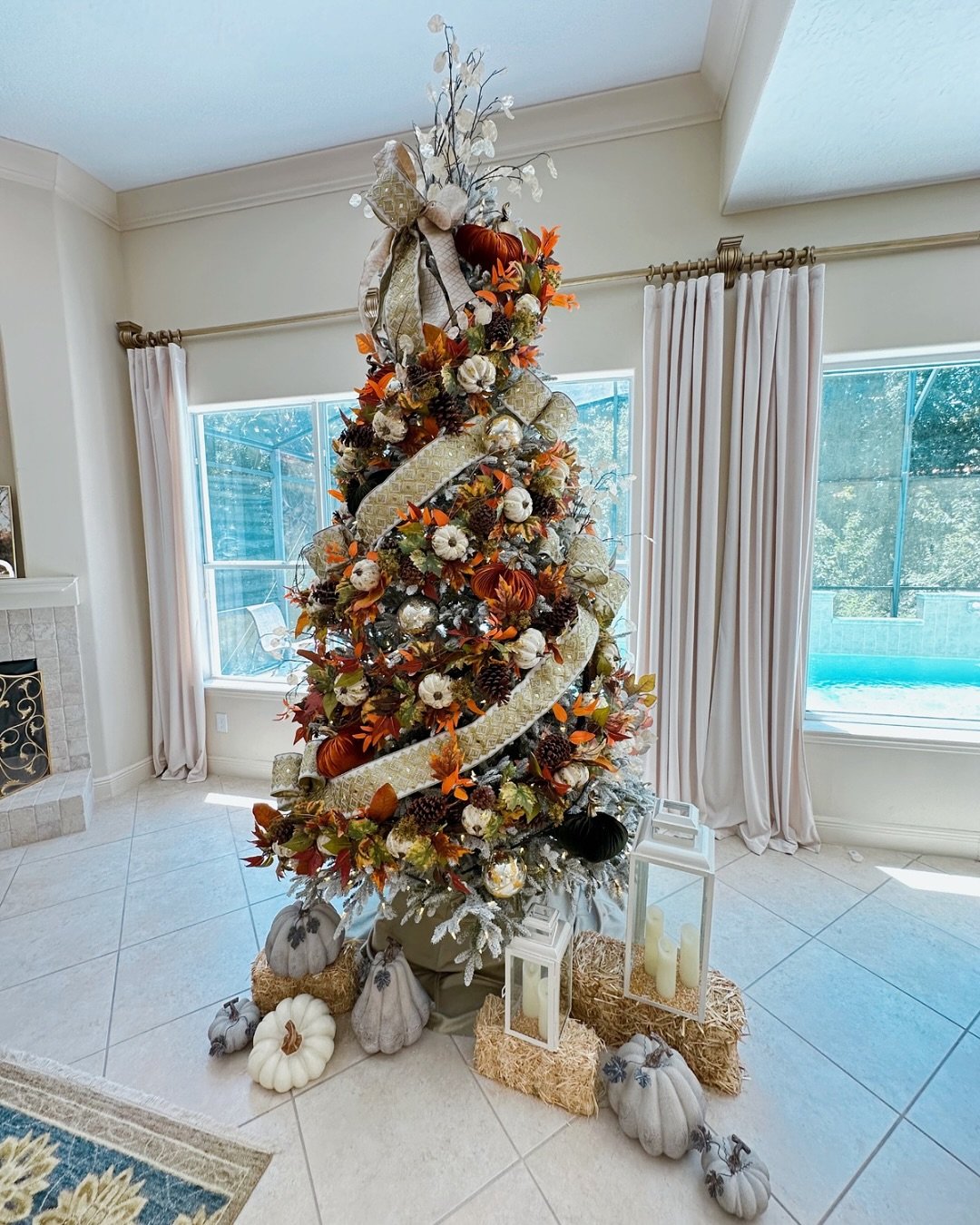 A unique Christmas tree decorated with fall elements like miniature pumpkins, autumn leaves, pinecones, and wide gold burlap ribbon.