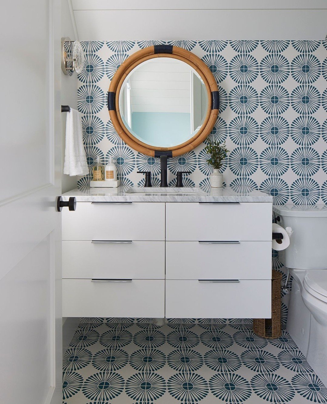 A small, white bathroom with a floating vanity, black fixtures, and a dramatic bohemian or starburst patterned tile on both the floor and the accent wall behind the vanity.
