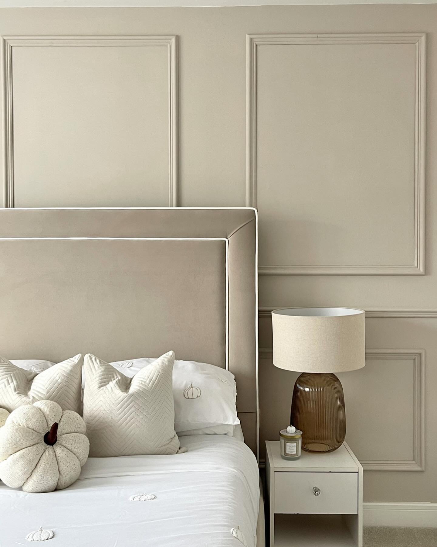 A modern bedroom with a large, ribbed amber glass lamp and a light linen shade on a white nightstand.