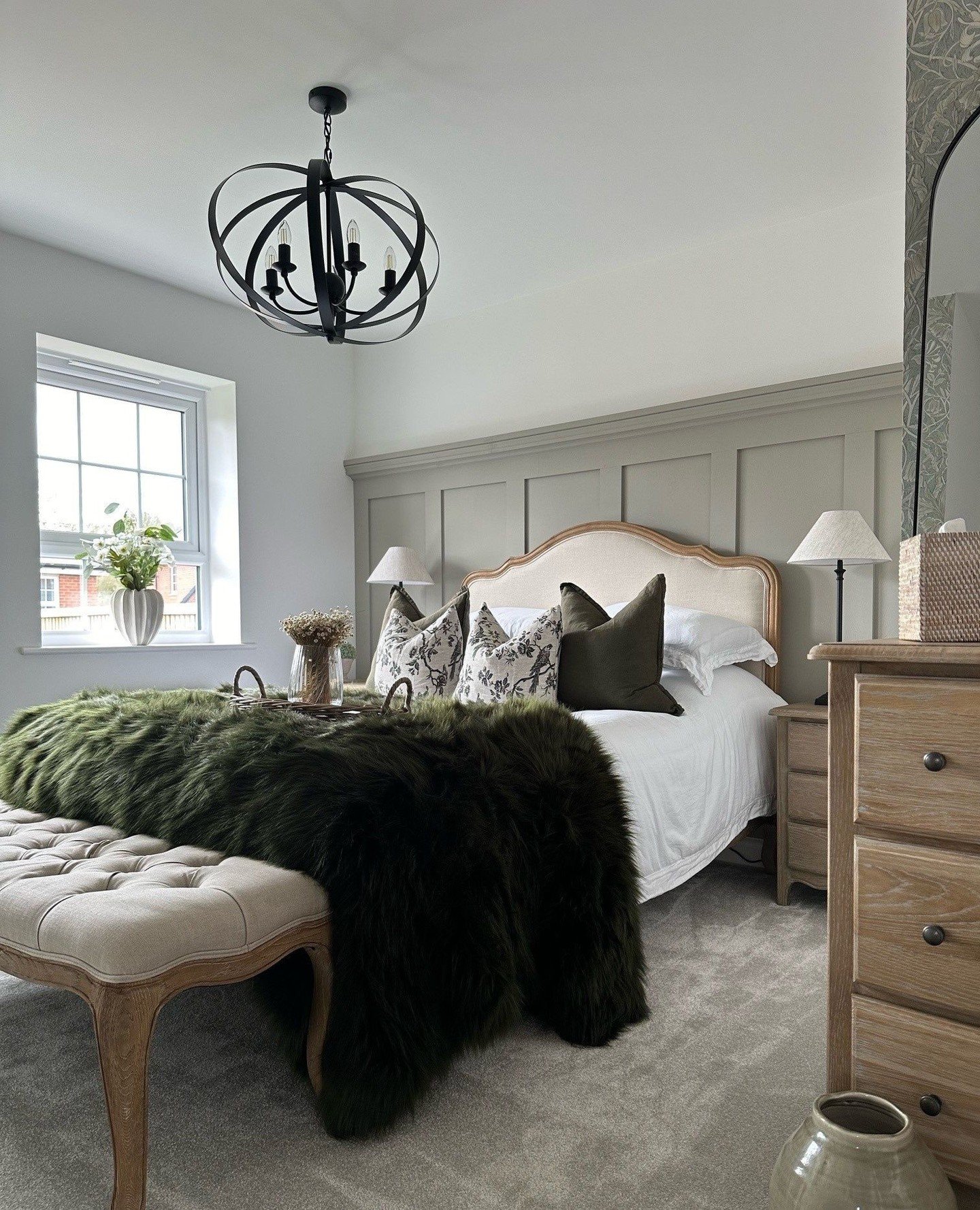 A rustic black orb chandelier with a four-bulb candelabra inside hangs from a chain over a bed in a farmhouse-style bedroom.