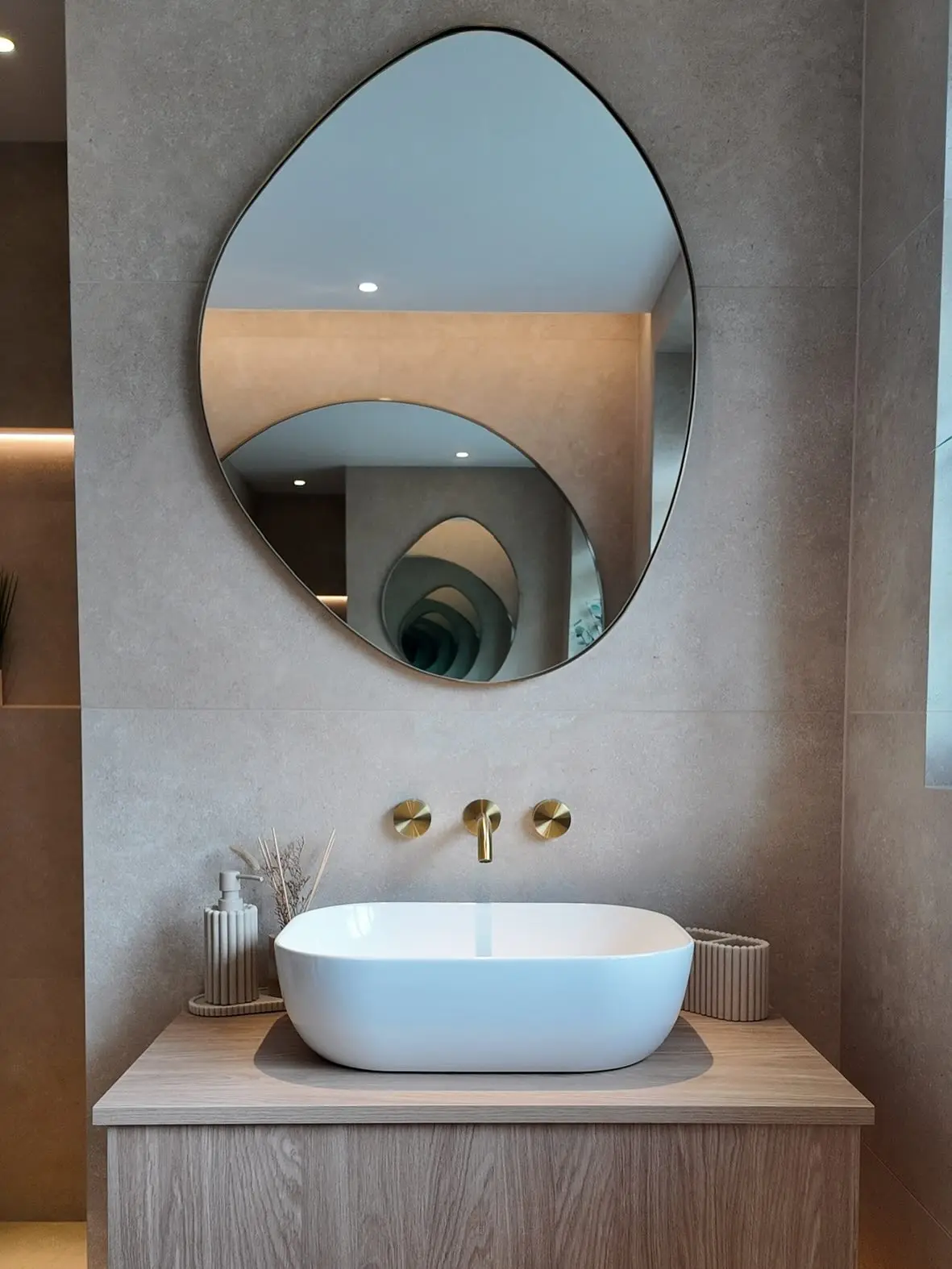 A modern bathroom with a uniquely shaped mirror featuring an etched swirl design, placed above a wood vanity and a white vessel sink.
