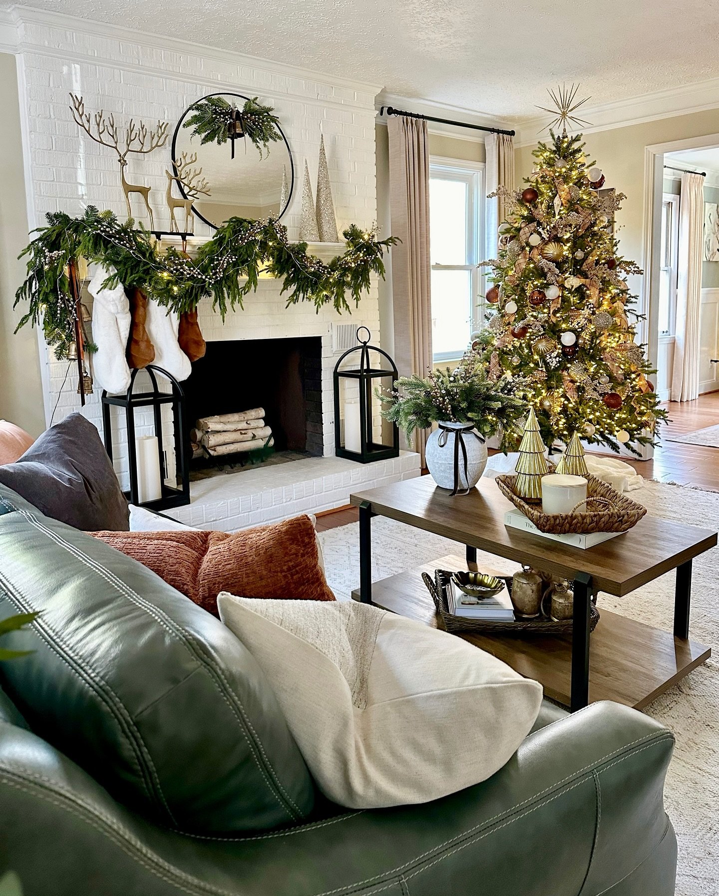 Living room with a white painted brick fireplace, a dark leather sofa, and a large Christmas tree decorated in gold and terracotta.