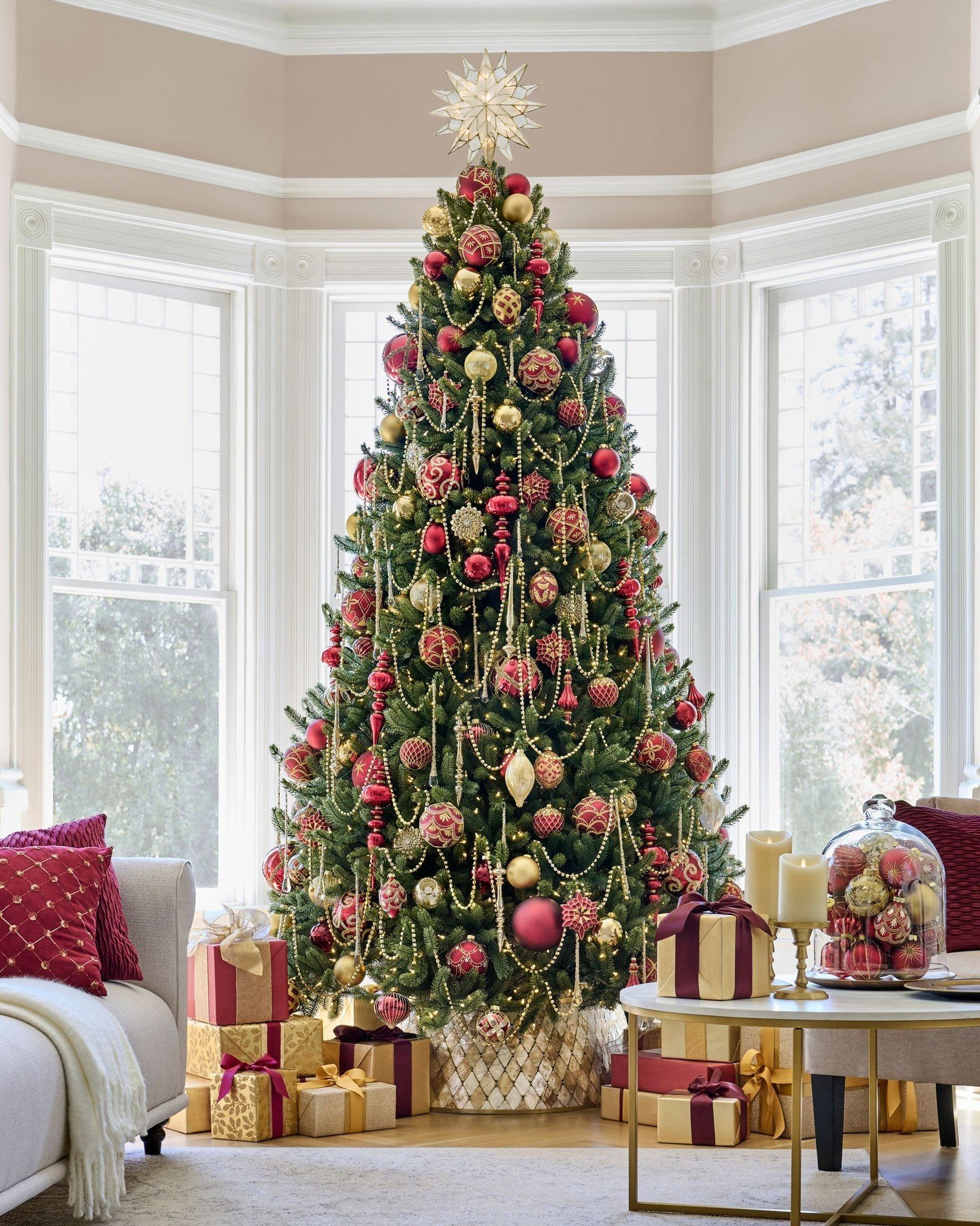 A lavishly decorated Christmas tree in a bay window, draped in gold and deep red ornaments and beaded garland.