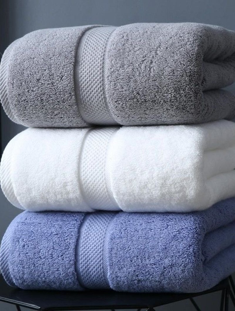 Stack of three thick, rolled bath towels in grey, white, and slate blue, showing a textured central band