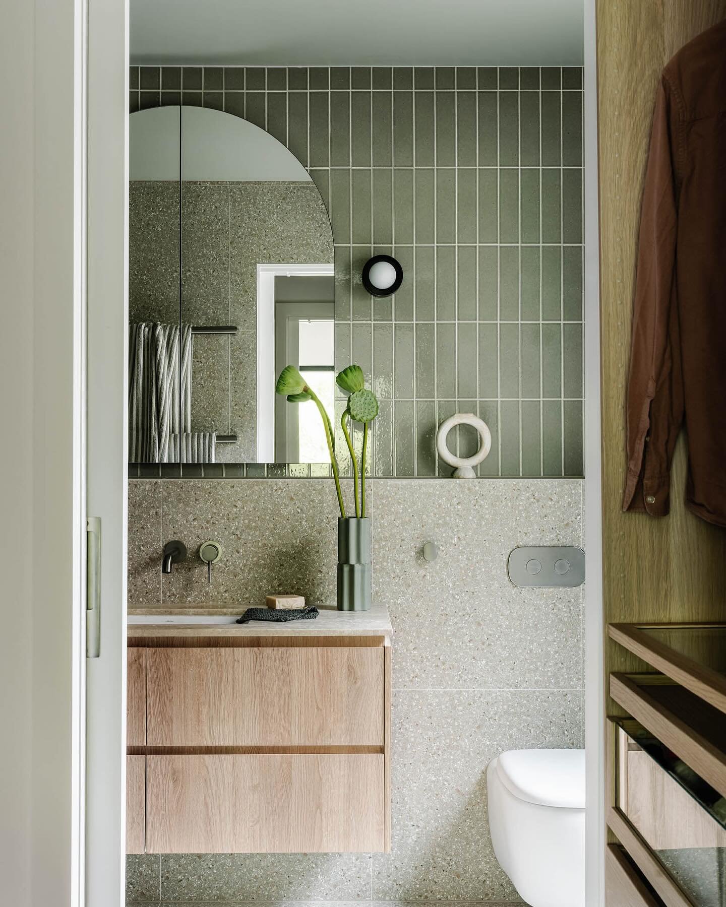 A small, modern bathroom with a light-wood floating vanity, a gray-green subway-tiled feature wall, and speckled gray terracotta tiles on the lower half and floor.