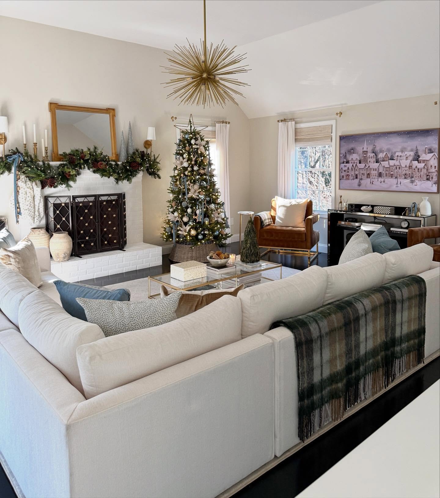 Large living room featuring a white sectional, decorated tree, and a fireplace with a garland and white brick surround.