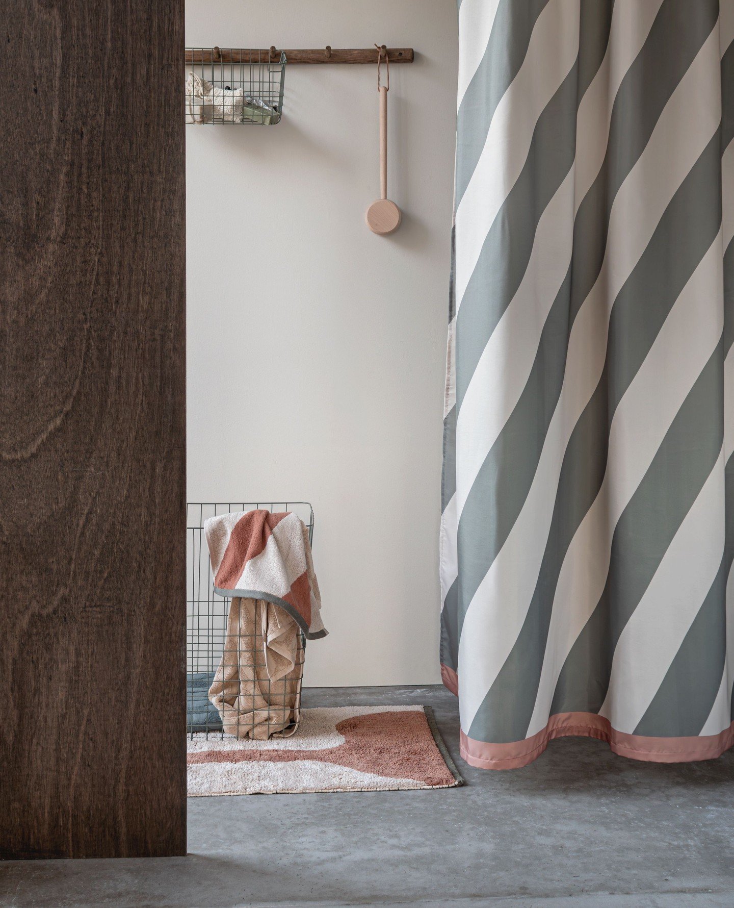 A shower curtain with wide, straight diagonal stripes in sage green and off-white, trimmed with a dusty rose band.