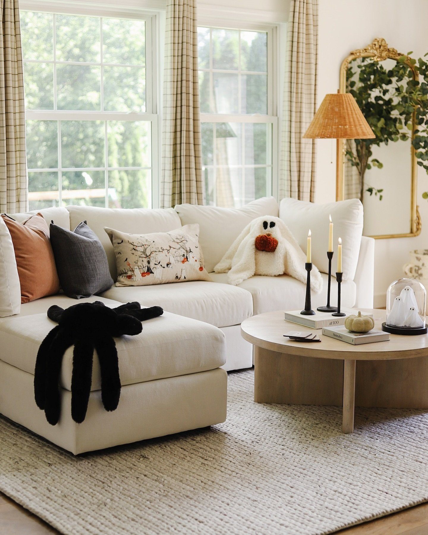 Living room with a white sectional sofa, a black furry spider blanket, a ghost pillow, and ghost decorations on a coffee table.