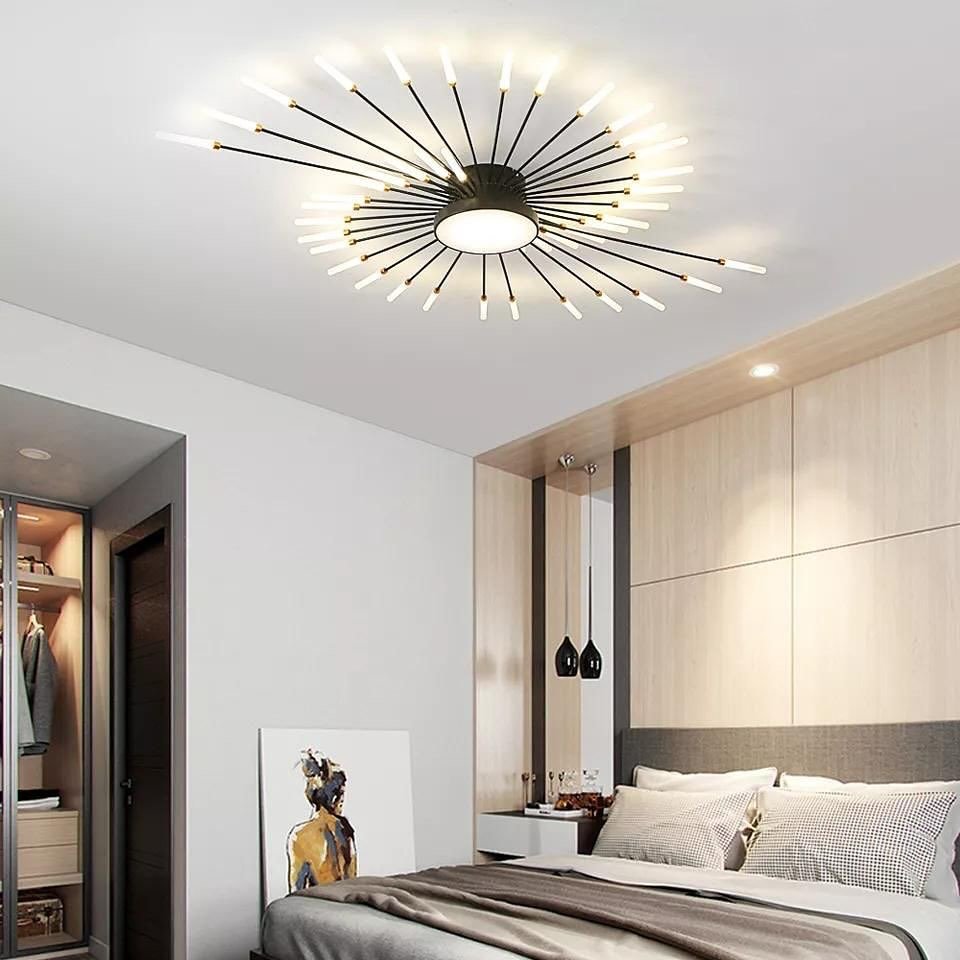 A contemporary starburst-style flush mount ceiling light with multiple gold and black arms radiating outwards is centered over a modern bed.