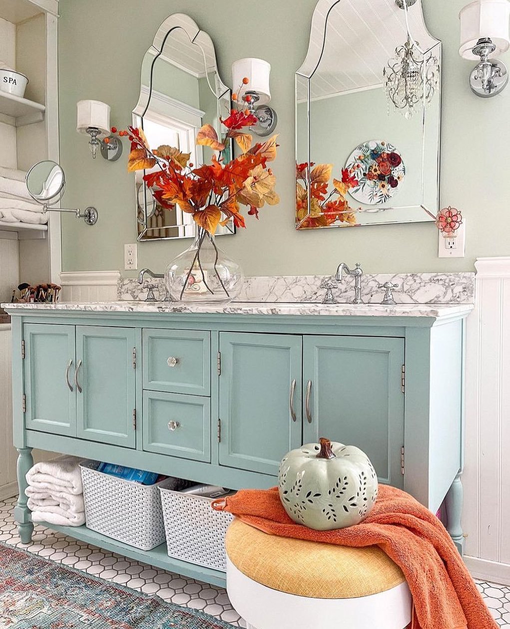 A mint green bathroom vanity with ornate mirrors and a vase of orange and red autumn leaves.