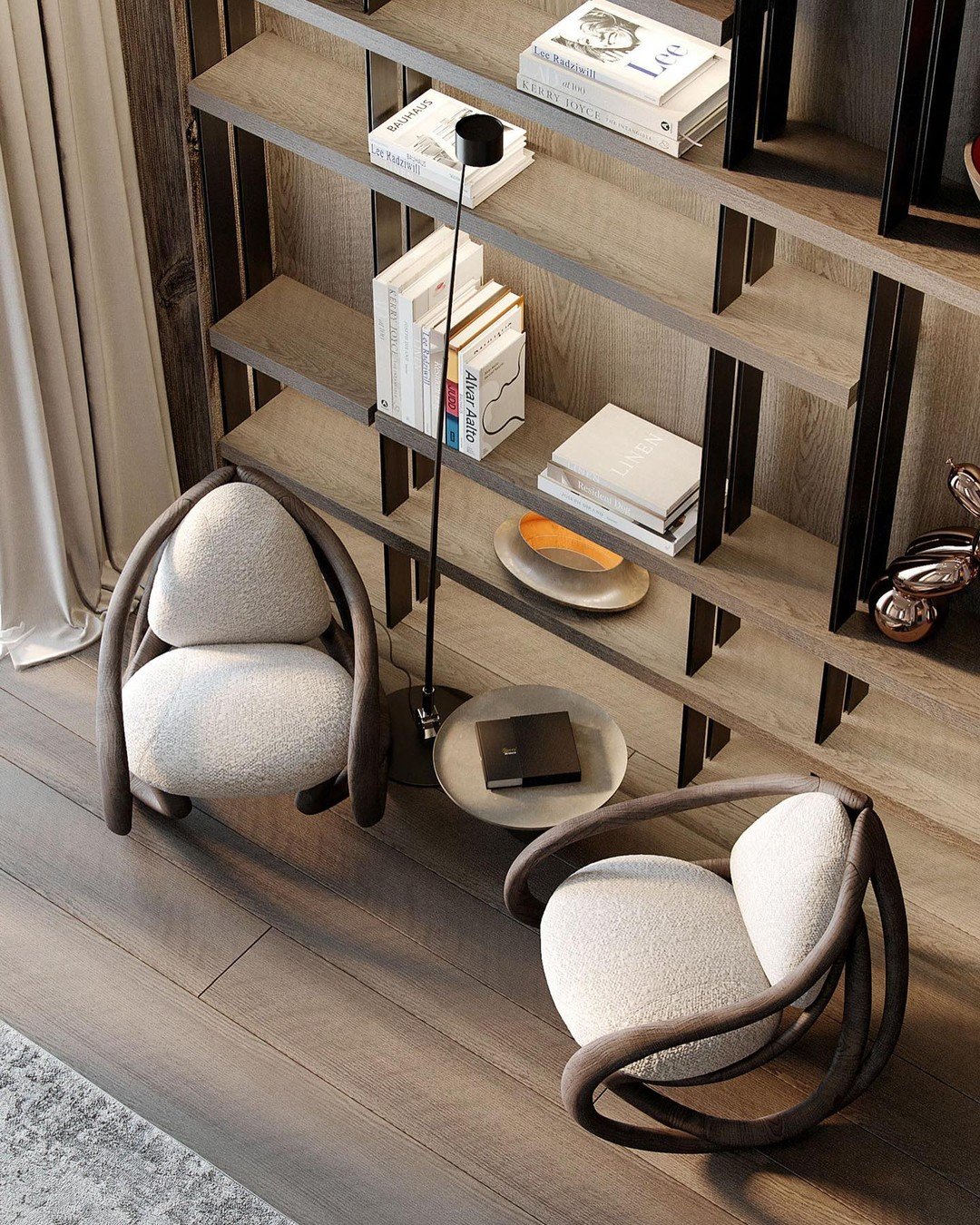 A pair of unique, low-profile armchairs with curved wooden frames and light upholstery sit on a wooden floor in front of a large bookshelf.