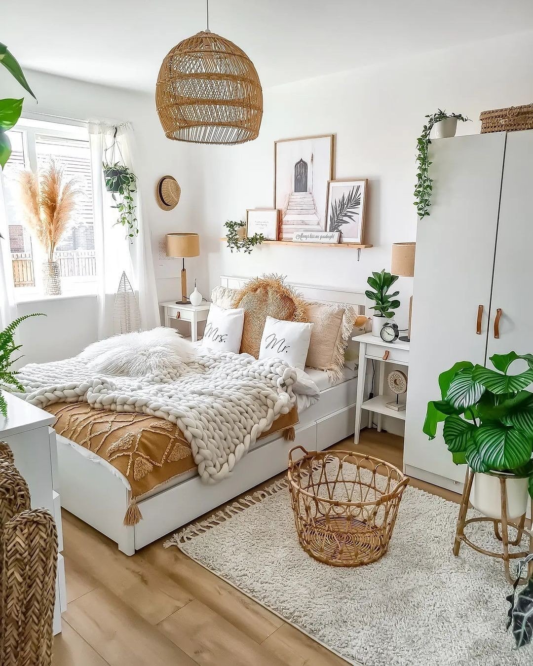 A bright, white boho bedroom with a mix of neutral tones, a large chunky knit throw blanket, and a variety of plants.