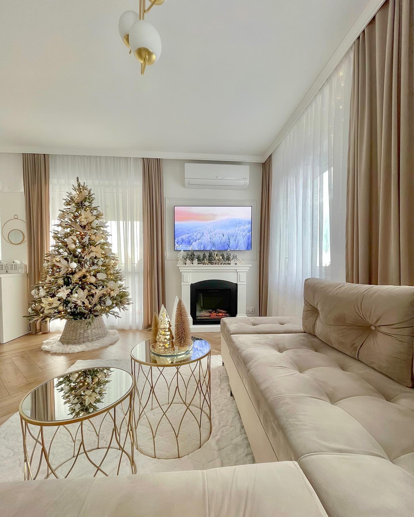Bright living room with a neutral velvet sectional, white fireplace, and a Christmas tree decorated in gold and champagne colors.