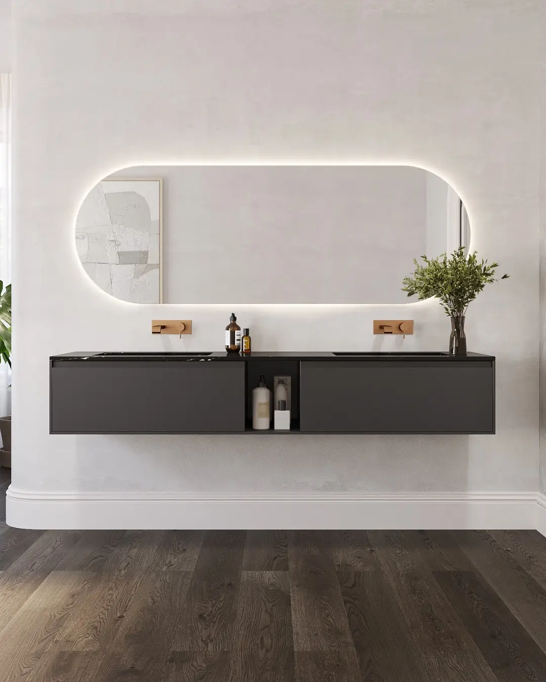 A dark gray floating double vanity with a black marble countertop and gold fixtures, centered below a large horizontal pill-shaped LED backlit mirror, set against a light-colored textured wall.