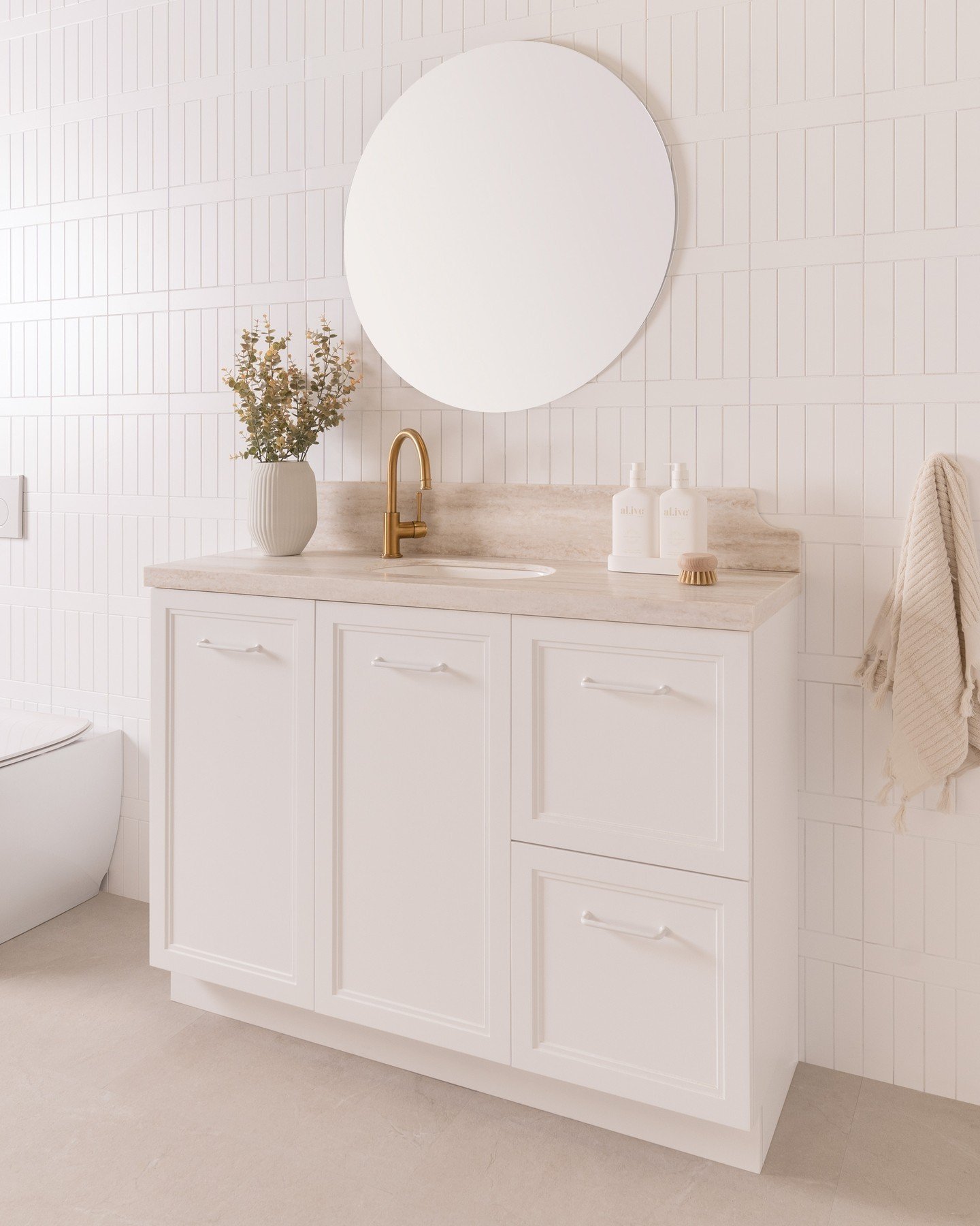 White, Shaker-style vanity with a light marble countertop, gold faucet, a large center cabinet, and two stacked drawers on the right.