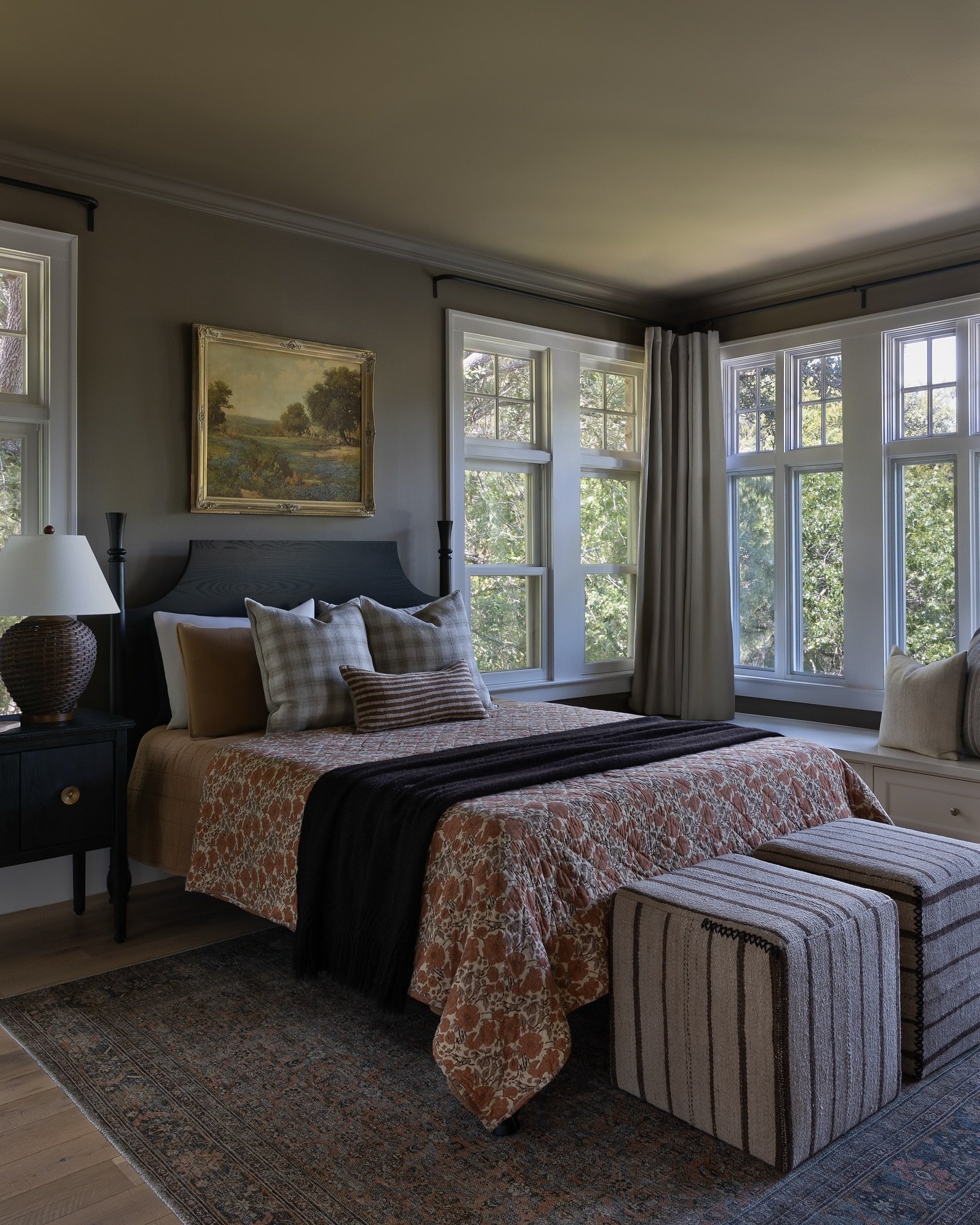 A cozy bedroom with dark gray walls, a patterned quilt, and a window seat overlooking a lush outdoor view.