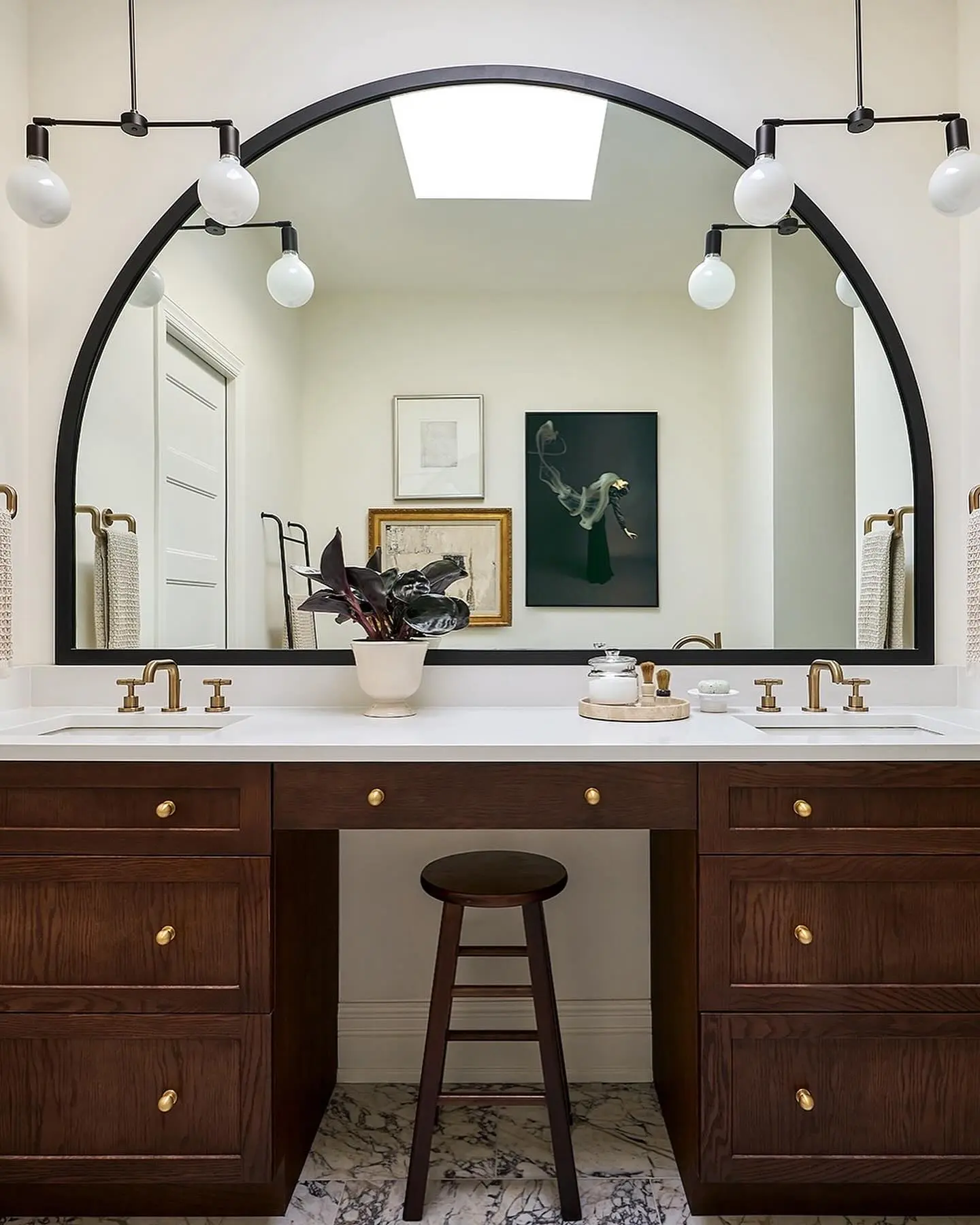 A contemporary bathroom with a large, arched black-framed mirror centered over a double sink vanity.