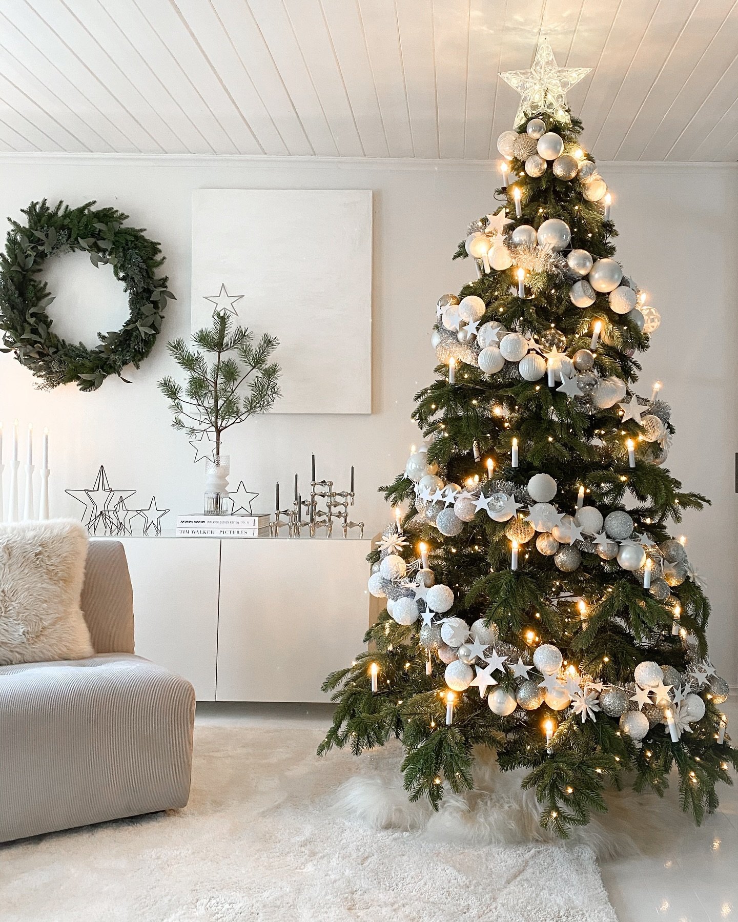 A Christmas tree decorated in a contemporary style with silver and white ornaments, paired with clip-on candle lights and a fuzzy white tree skirt.
