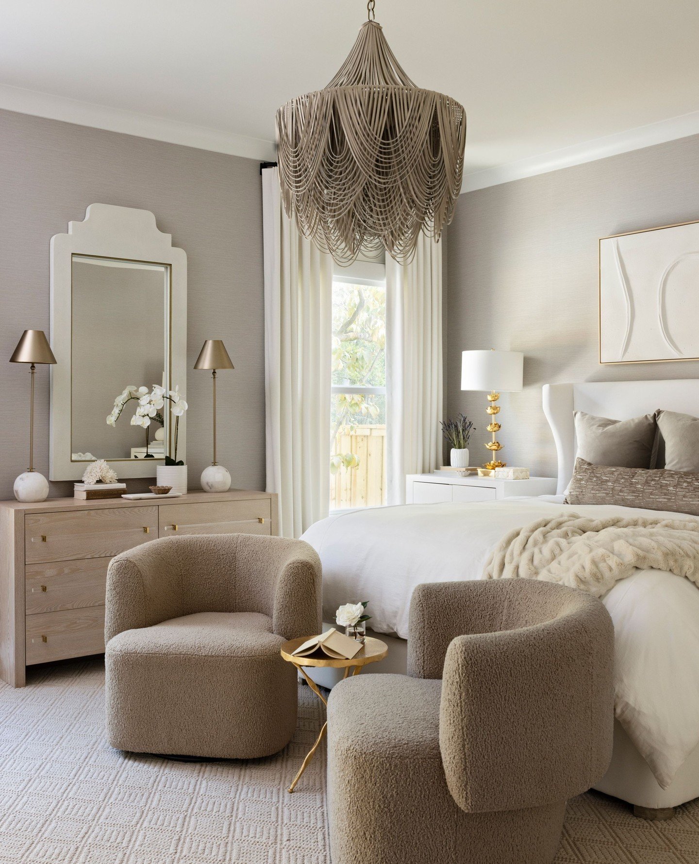 A pair of small, textured teddy-like armchairs with a golden side table between them sit at the end of a bed.