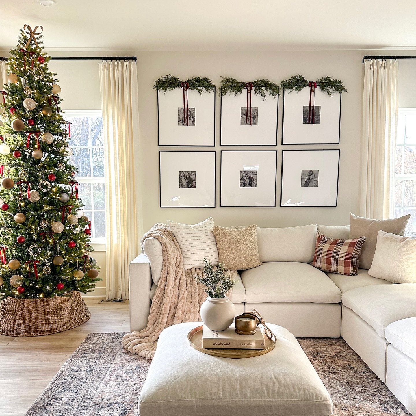 Cozy living room with a white sectional, large Christmas tree in a basket, and a gallery wall decorated with pine boughs.
