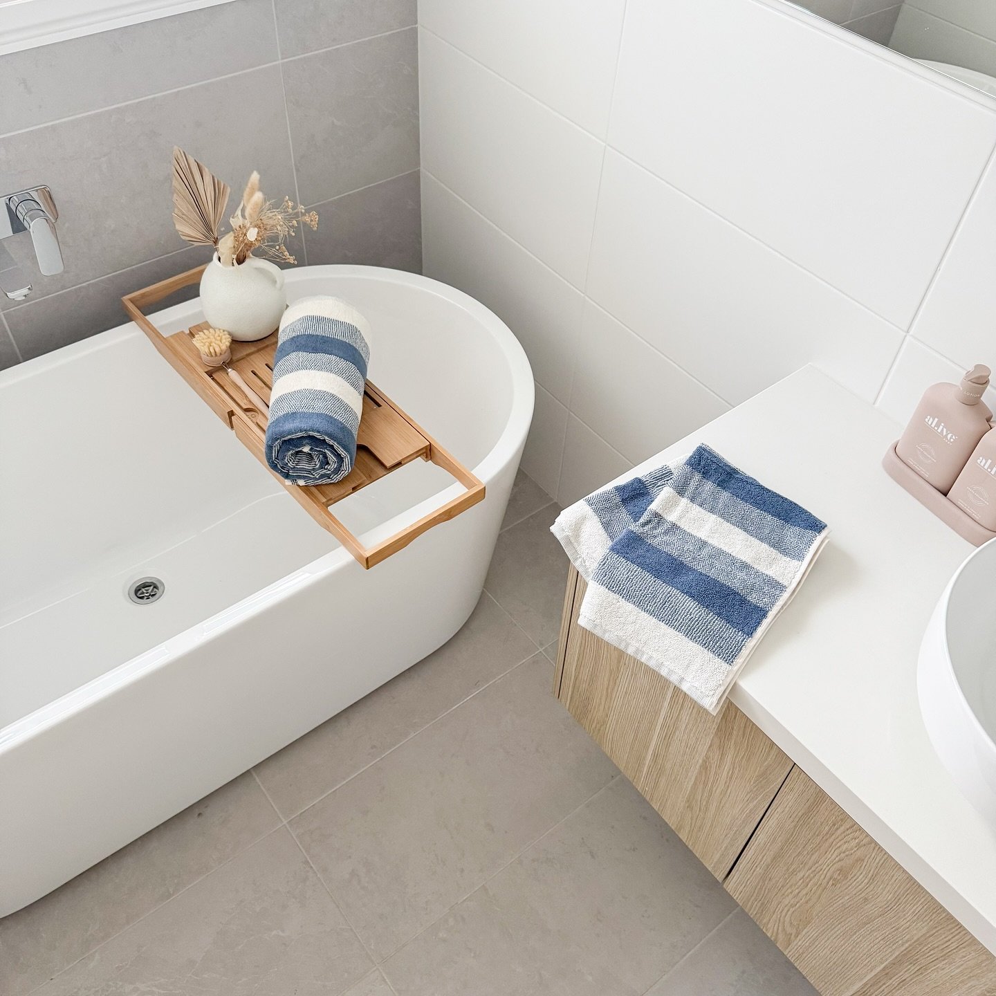 Blue and white striped towel rolled on a bamboo bath caddy in a modern bathroom with light grey tile.