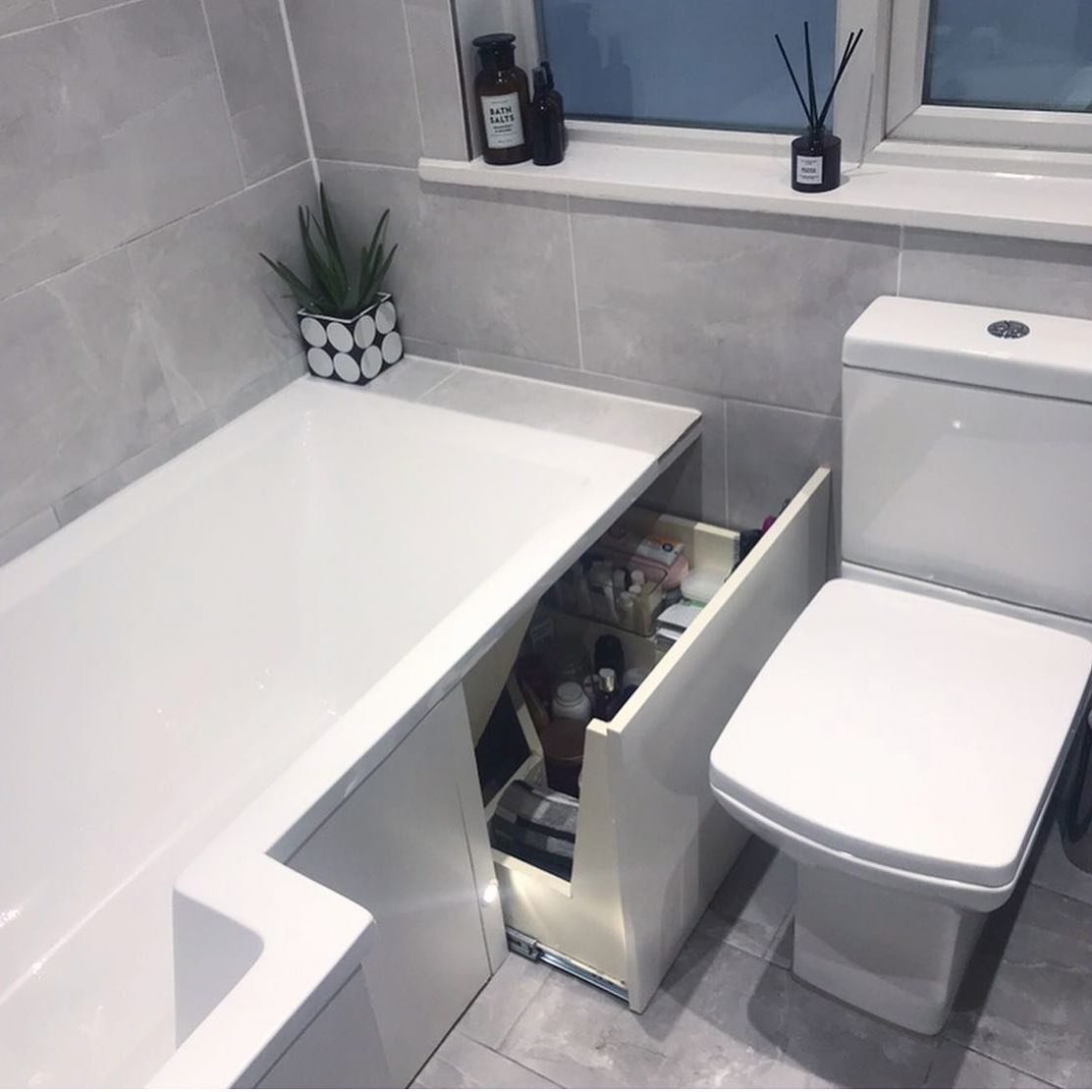 White bathtub with a built-in pull-out drawer system integrated into the end bath panel, used for storing bottles and toiletries next to a toilet.