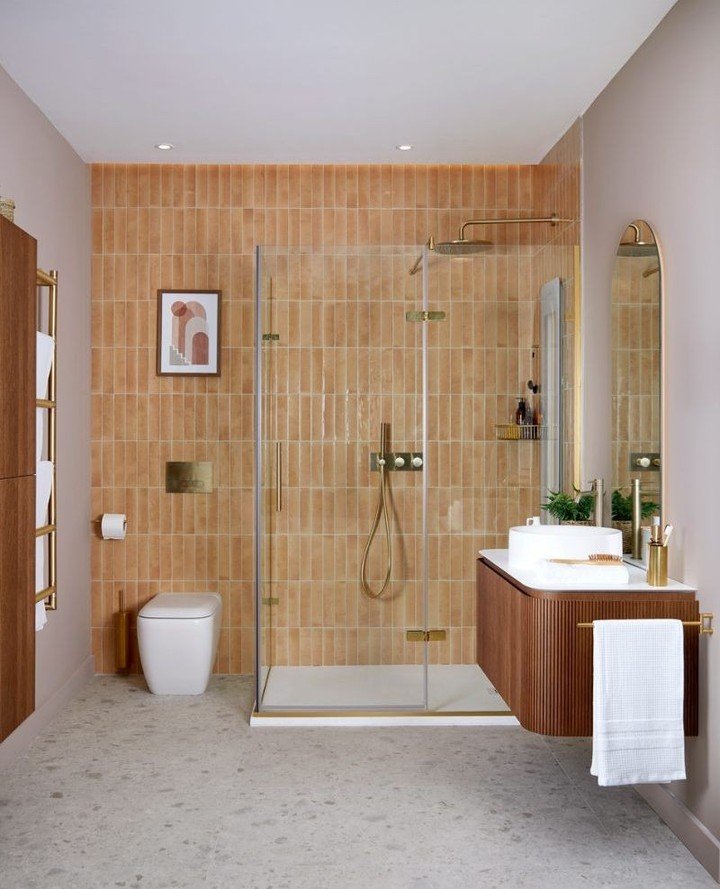 A contemporary shower recess featuring vertical, handmade-look terracotta subway tiles and brass/brushed gold fixtures, flanked by neutral painted walls.