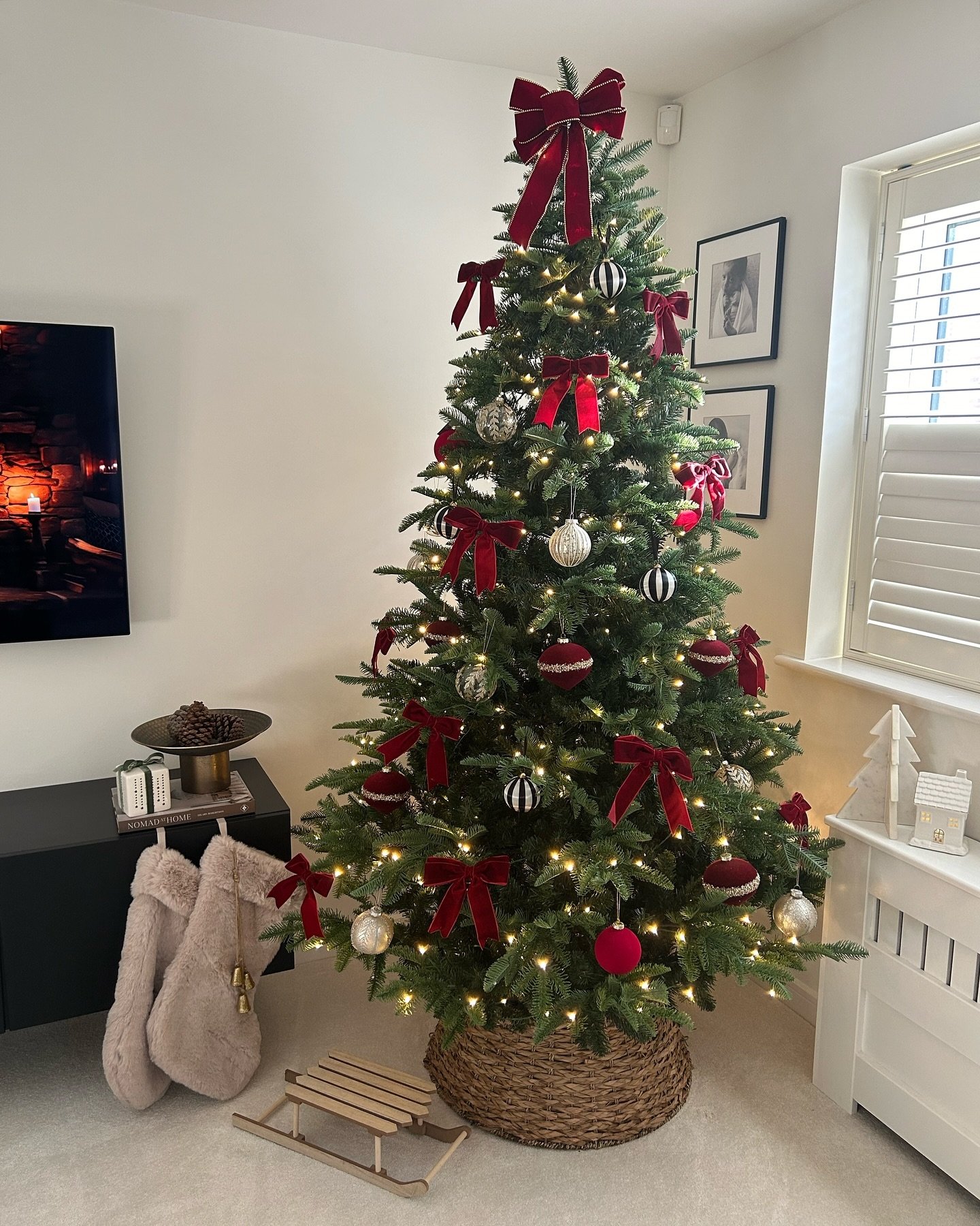 A slender Christmas tree decorated primarily with plush red velvet bows and a mix of white-and-black and burgundy ornaments.