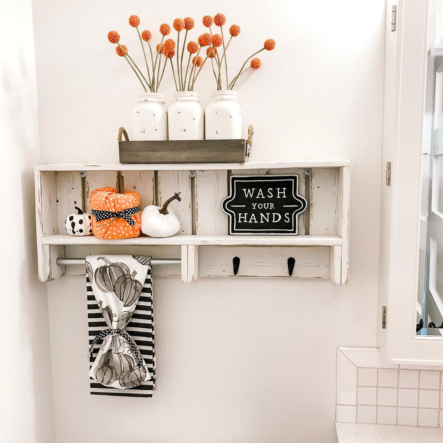 A white rustic shelf in a bathroom decorated with pumpkins and orange floral stems.
