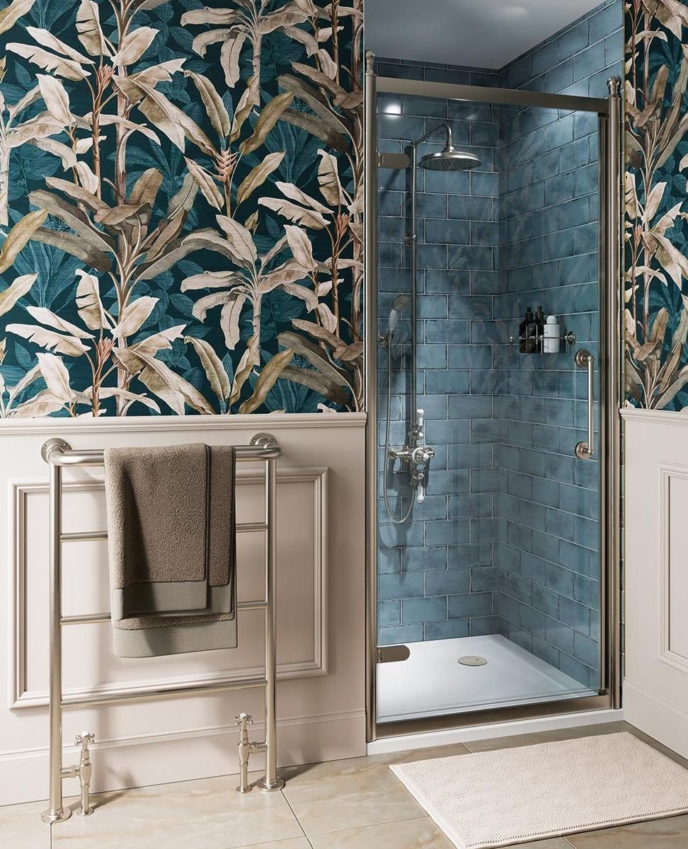 A luxurious shower area featuring moody, handmade-look teal subway tiles set against botanical print wallpaper and chrome fixtures.