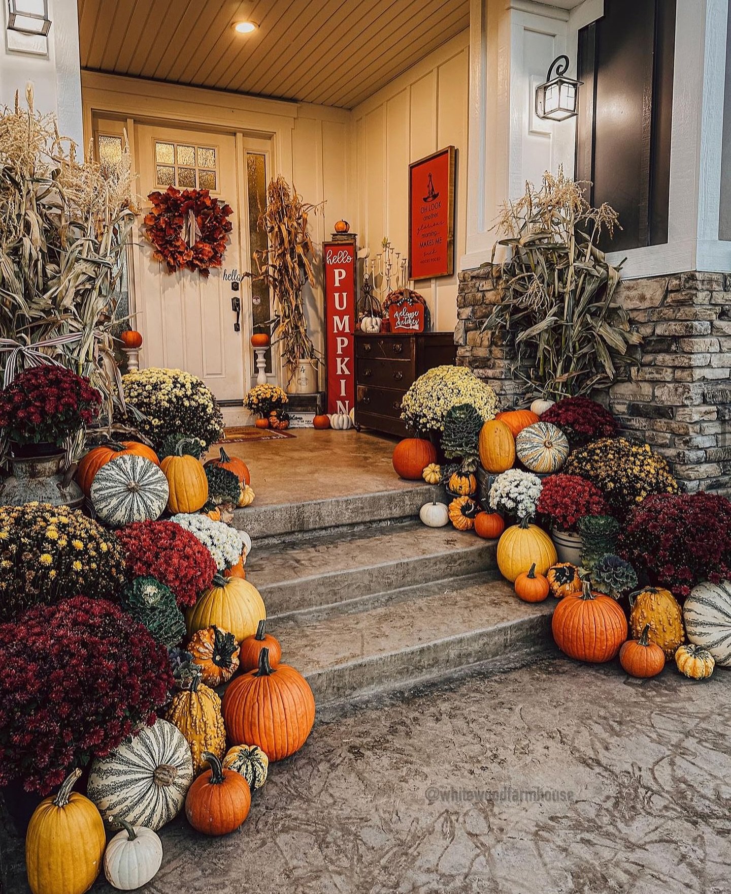 A bountiful farmhouse porch decorated for fall with a large collection of pumpkins, gourds, mums, and dried corn stalks on the stairs.