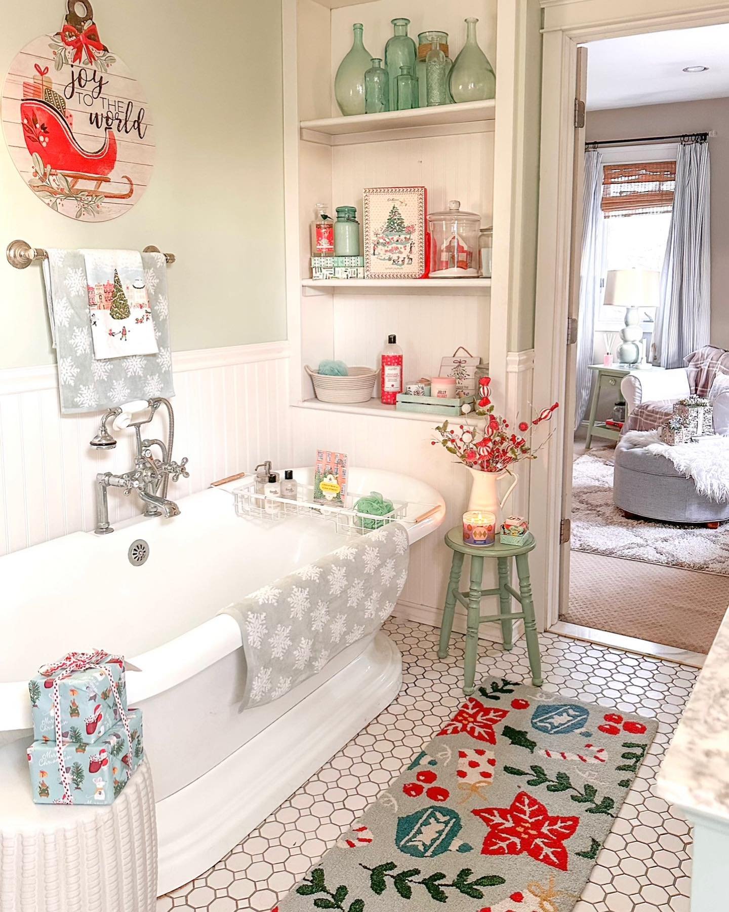 A mint green and white bathroom with a clawfoot tub, holiday signs, snowflake towels, and a bold Christmas patterned rug on honeycomb tile.