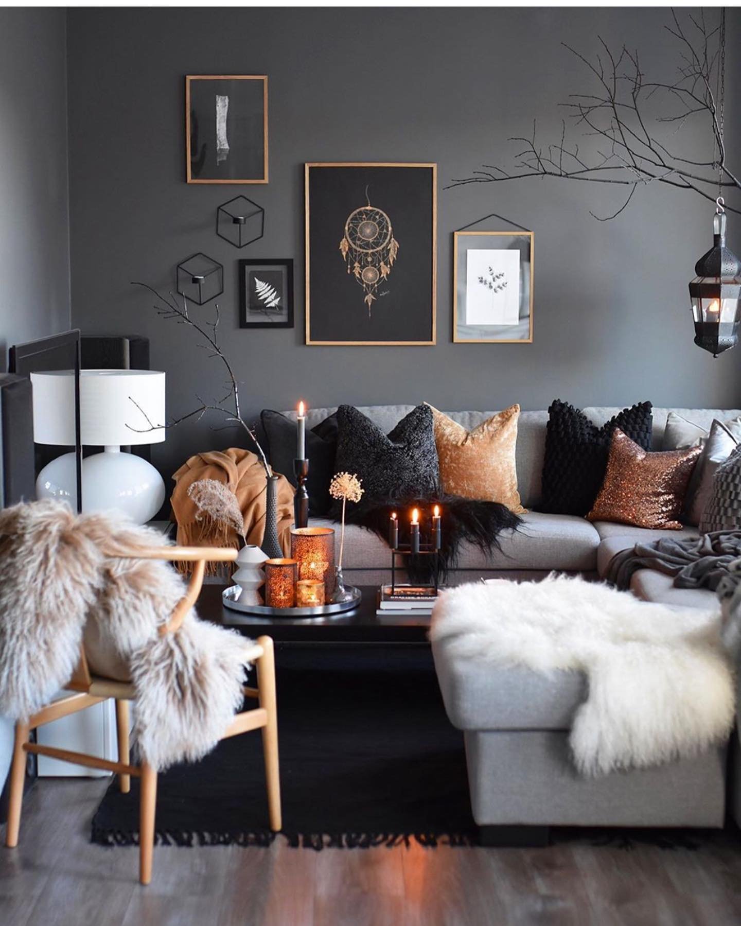 Dark living room with a gray sectional sofa, faux fur throws, and a gallery wall with a dreamcatcher print.