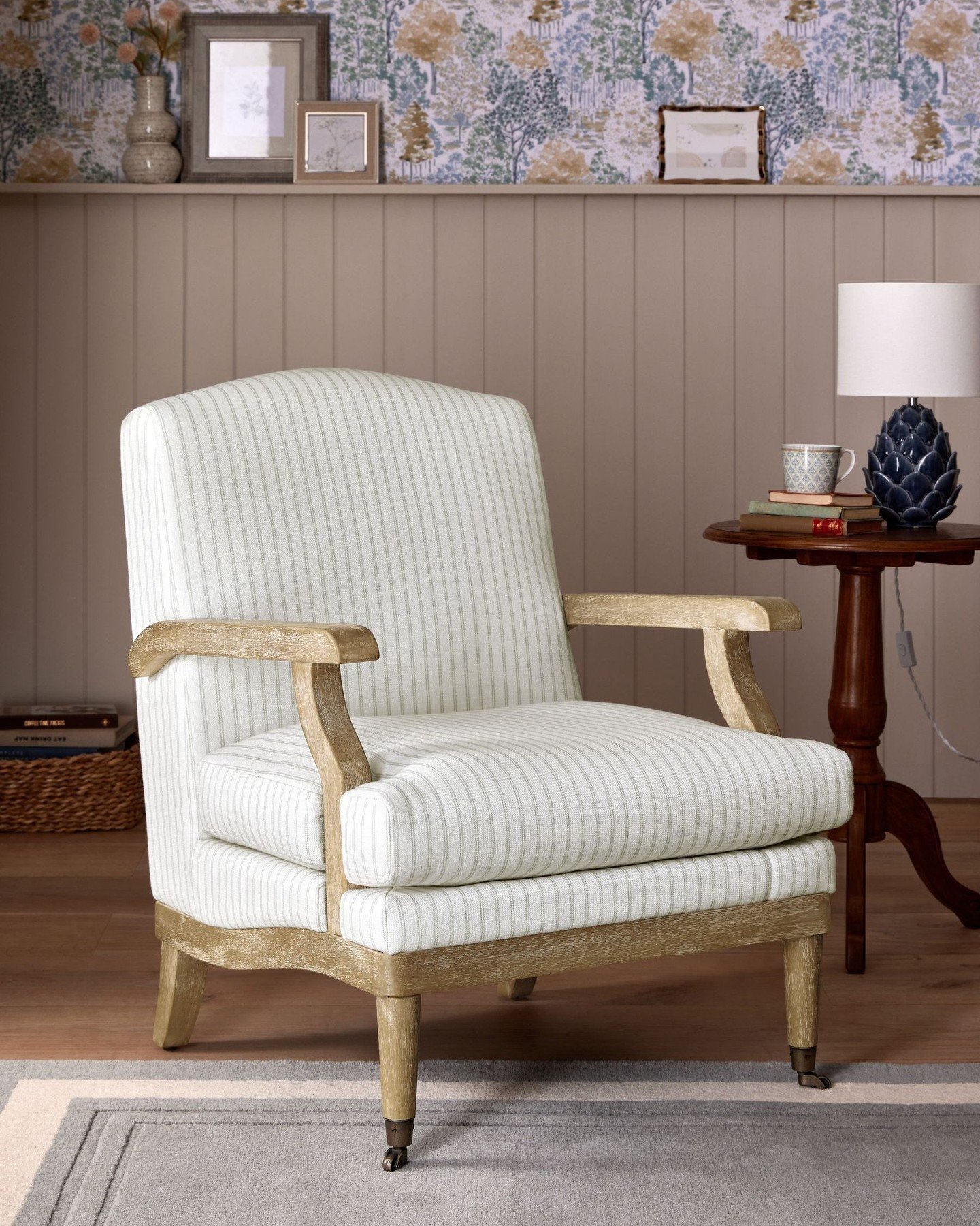 A classic French-style armchair with a distressed wooden frame and pinstriped upholstery sits on a wooden floor.
