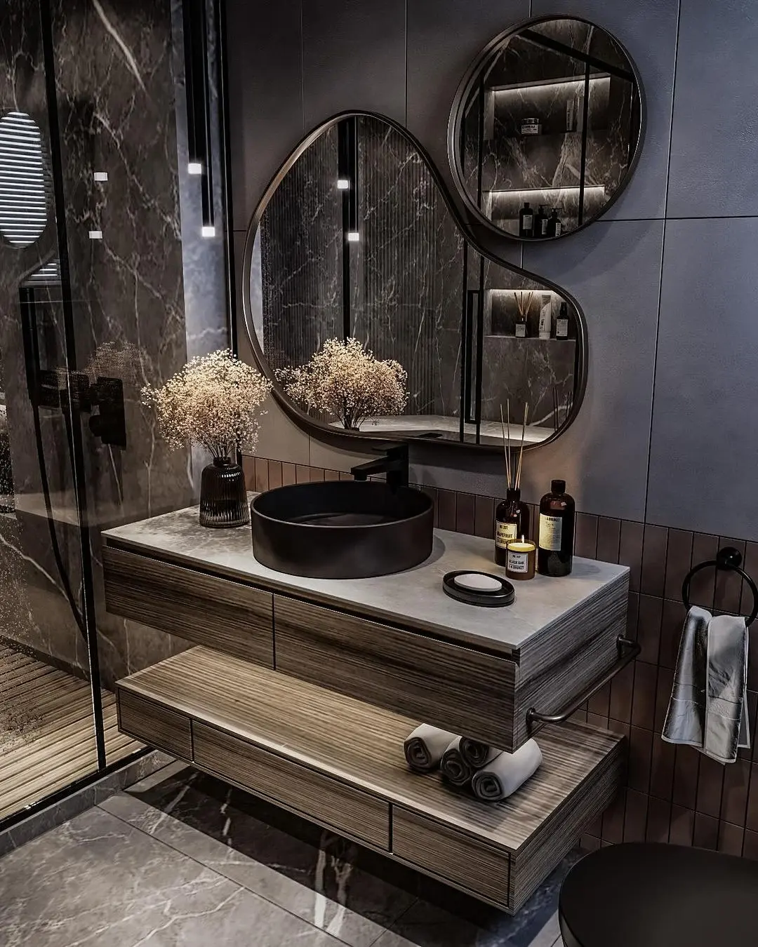 A modern bathroom with a trio of abstract-shaped mirrors with dark frames, positioned above a floating wood vanity with a black sink.