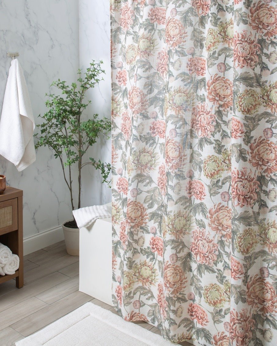 A white shower curtain with a large-scale, repeating floral pattern of chrysanthemums in muted coral, blush, and sage green tones.