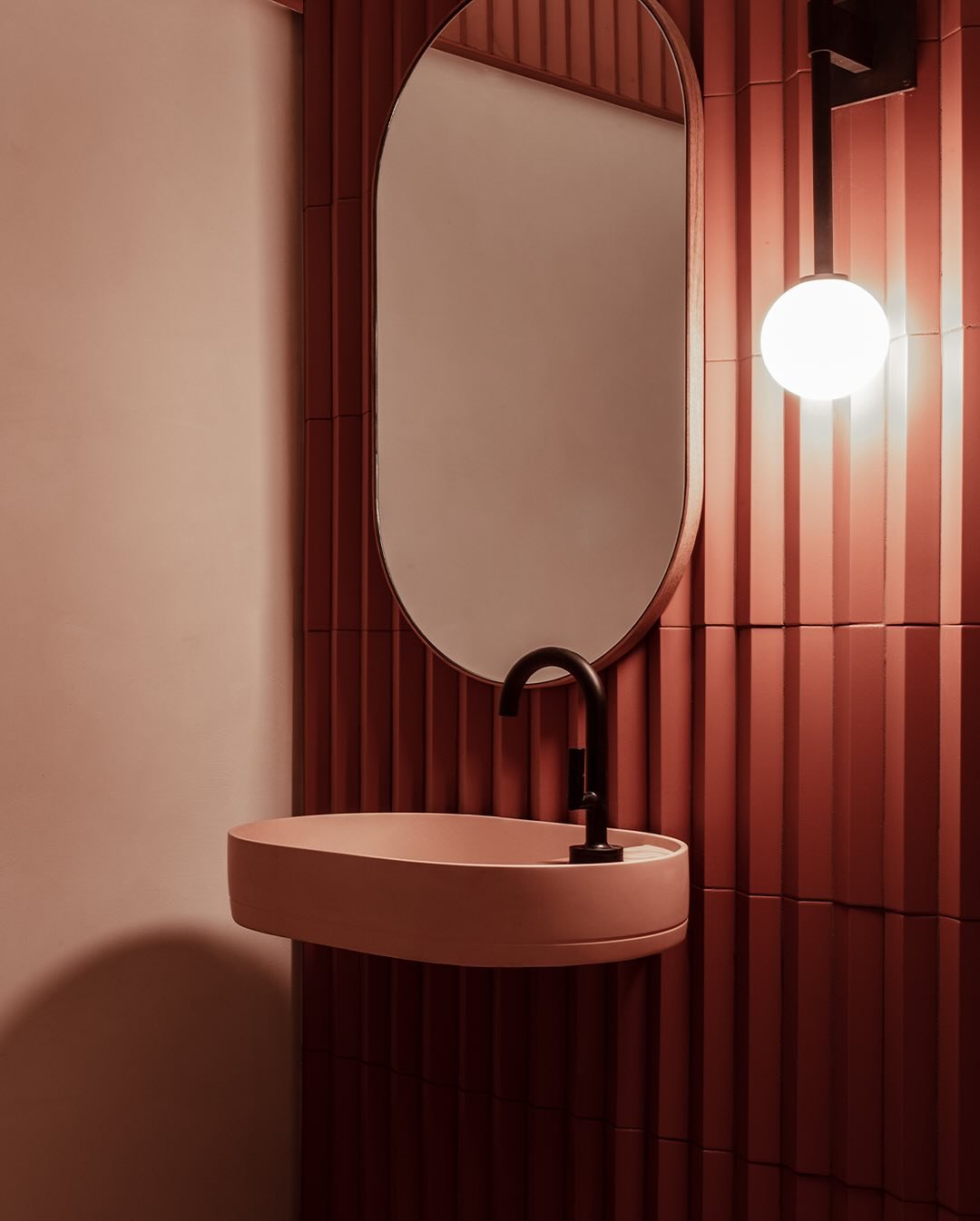 A small bathroom with a minimalist blush pink floating sink and a matte black faucet.