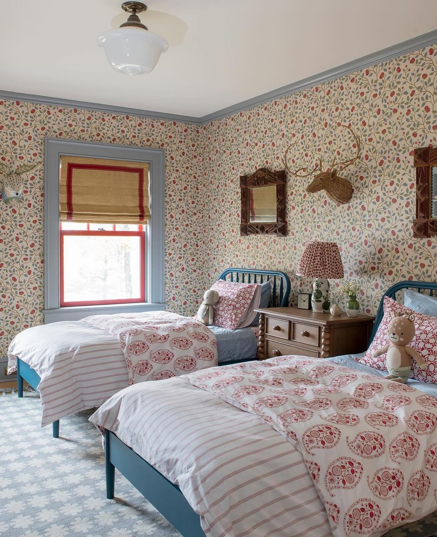 A vintage-style twin bedroom with floral wallpaper, blue metal beds, and red and white patterned bedding.