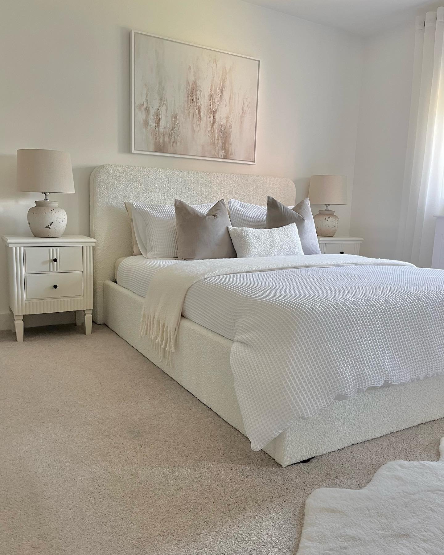 A minimalist all-white bedroom with matching ceramic lamps on either side of the bed.