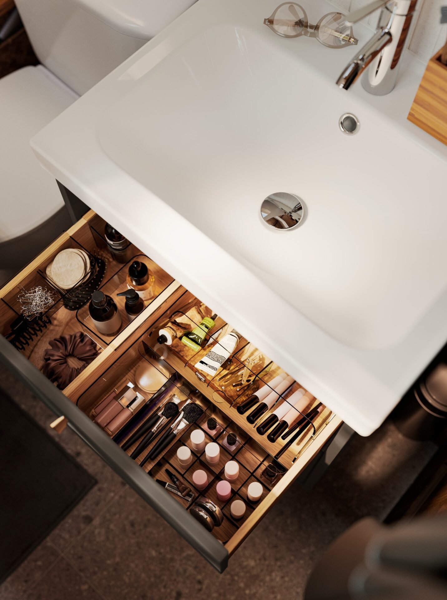 Overhead shot of an open deep vanity drawer beneath a sink, featuring wooden dividers and inserts used to neatly organize makeup, brushes, bottles, and hair accessories.