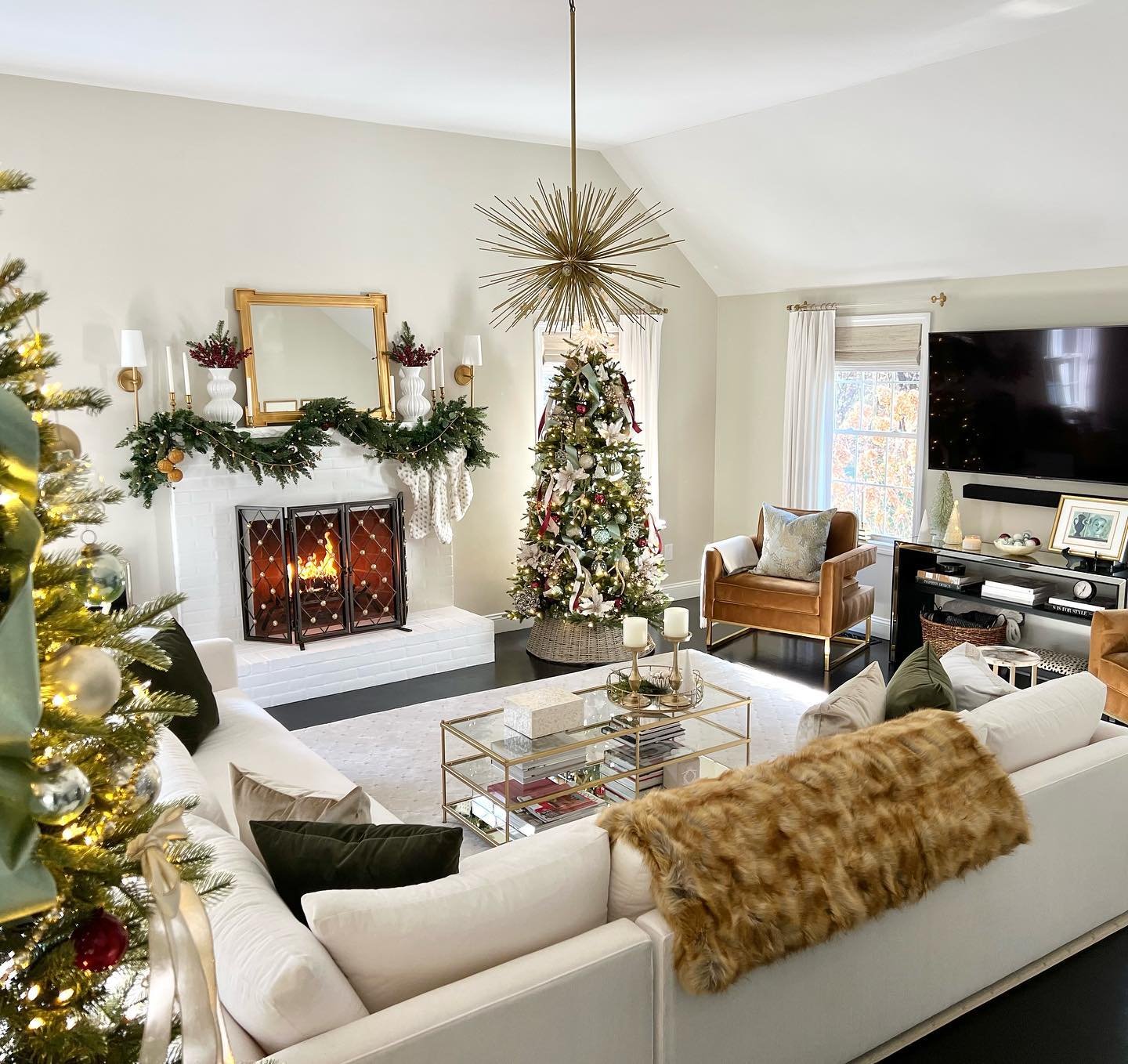 Spacious living room with a white sectional, decorated Christmas tree, starburst chandelier, and a cozy fireplace