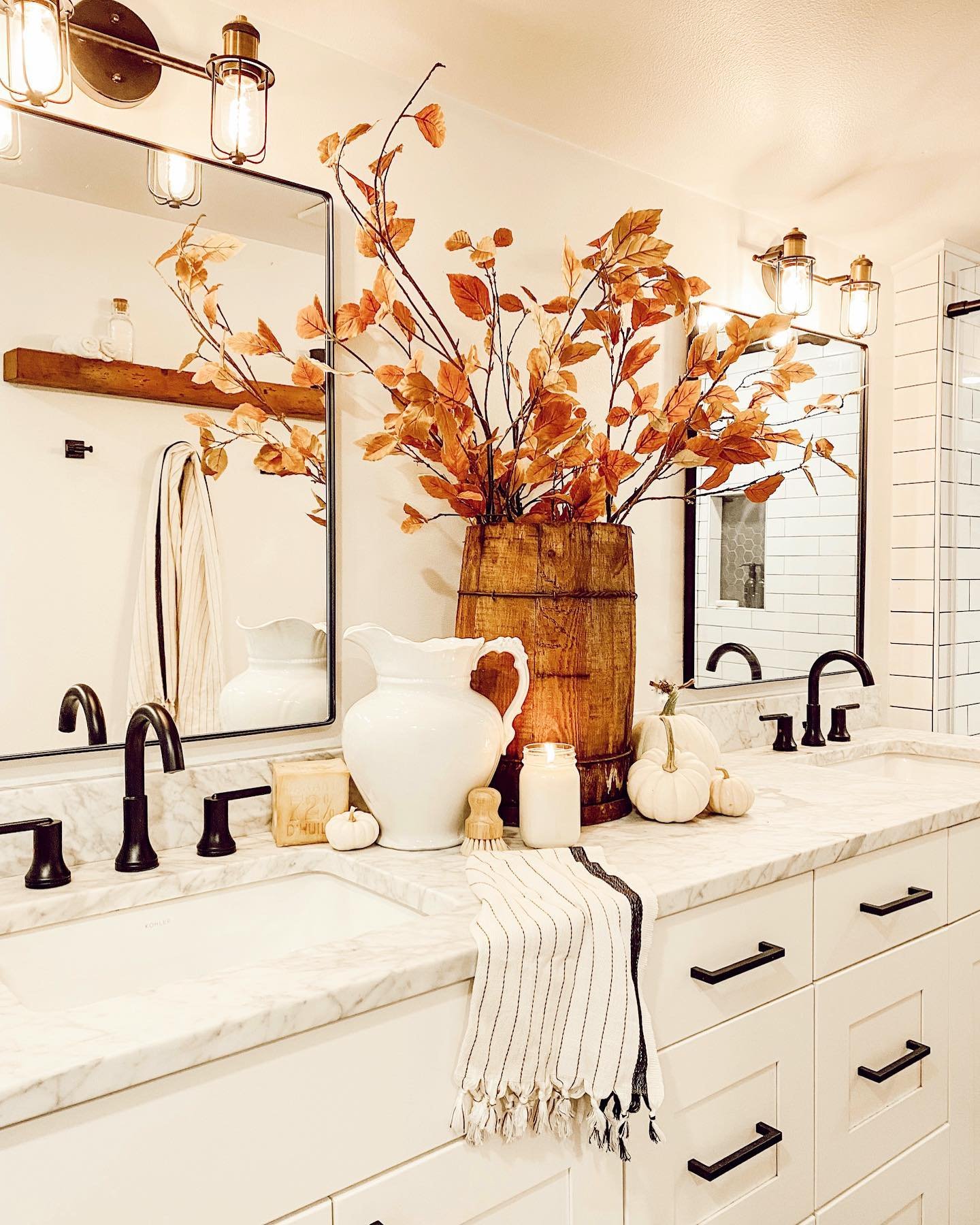 A double vanity in a modern bathroom with a large wooden bucket filled with tall, faux autumn branches.